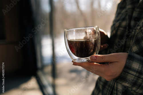 Closeup cropped shot of unrecognizable woman holding cup with hot aroma coffee in morning sunlight. Closeup of lady enjoying drinking coffee at home. Happy relaxed female drinking tea on kitchen.