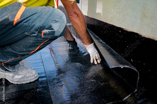 Photos Worker unroll foil with bitumen waterproofing installation over concrete