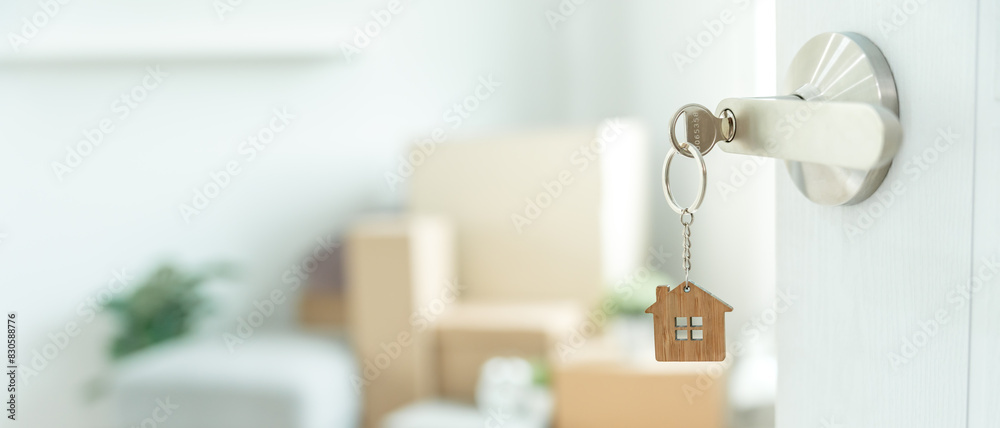 Fototapeta premium Moving house, relocation. The key was inserted into the door of the new house, inside the room was a cardboard box containing personal belongings and furniture. move in the apartment or condominium