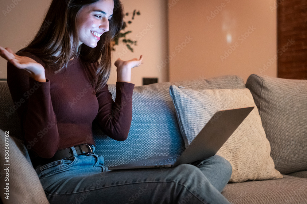 Obraz premium Happy brunette girl waving hand using laptop app enjoying online virtual chat video call in remote virtual meeting, relaxed and smiling talking in night with friends.