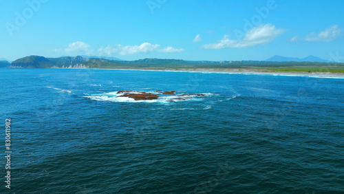 Aerial picturesque seascape with blue water, boulders rising up above sea surface. Clip. Summer coastline and blue sky above.