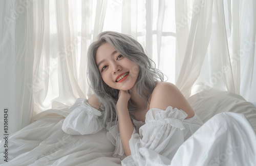 Beautiful Korean women with grey hair, smiling and posing on the bed in a white dress against a white curtain background © Kien