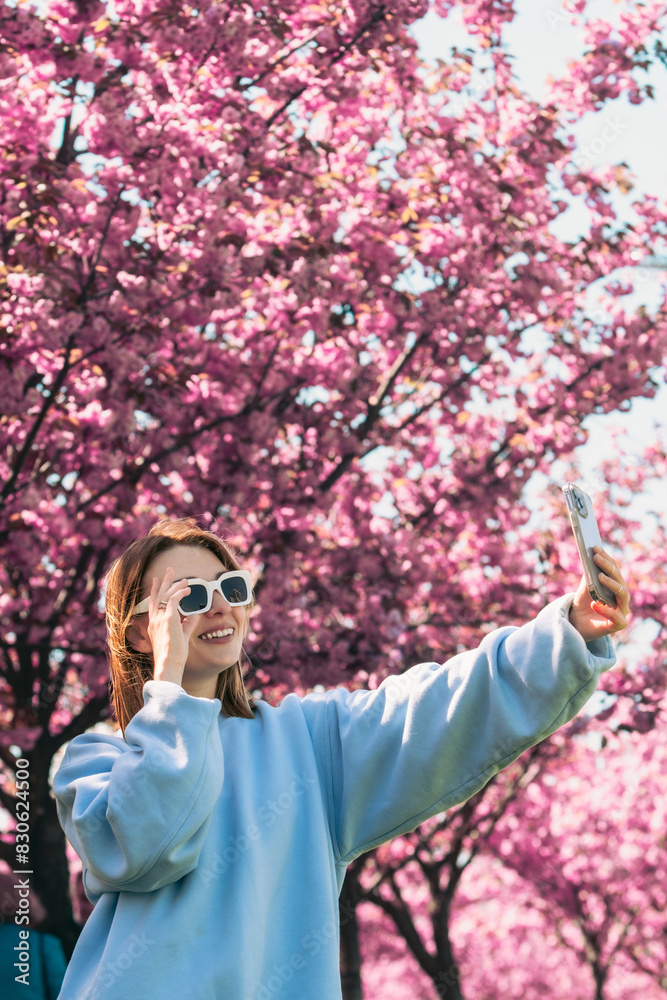 happy woman taking selfie on the phone in front of blooming sakura