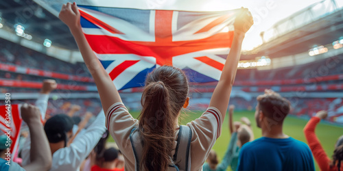 Cheering crowd at a football stadium. A fan waves the Union Jack flag, showing support and excitement during a thrilling match.