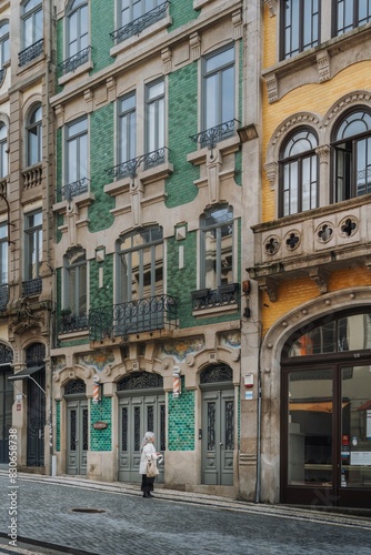 An elderly woman looks at the entrance door of a classic and typical Porto city building in the city center.