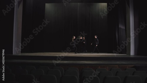 Side view of a group of confident and happy actors in black clothes in the theater going on stage near a black curtain during a rehearsal in an empty hall photo