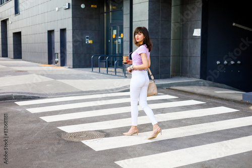 Attractive woman walking in city with coffee cup in hand. She is going on job, walking through the city streets and drinking take away coffee.