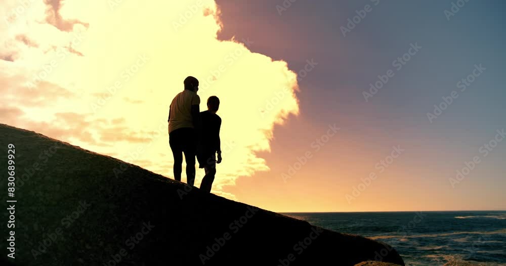 People, holding hands and fitness in sunset at beach with help on rocks, clouds and outdoor together. Men, support and lift by ocean, sea and silhouette with training, exercise or workout in summer