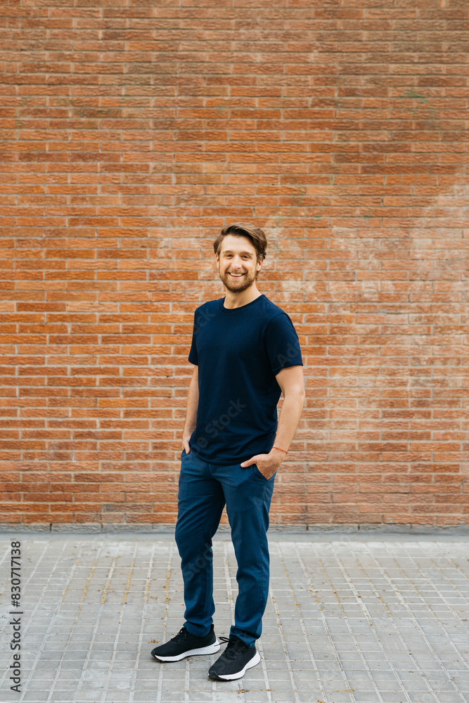 Portrait of a young man standing against a brick wall, smiling confidently with his hands in his pockets. He is dressed casually, appearing relaxed and approachable. Portrait of a young man standing against a brick wall, smiling confidently with his hands in his pockets. He is dressed casually, appearing relaxed and approachable.
