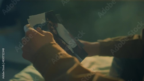 Side tilt footage of young Caucasian man sitting in bed at dawn looking at old photos of his friends or ex girlfriend and getting angry, throwing photos away photo