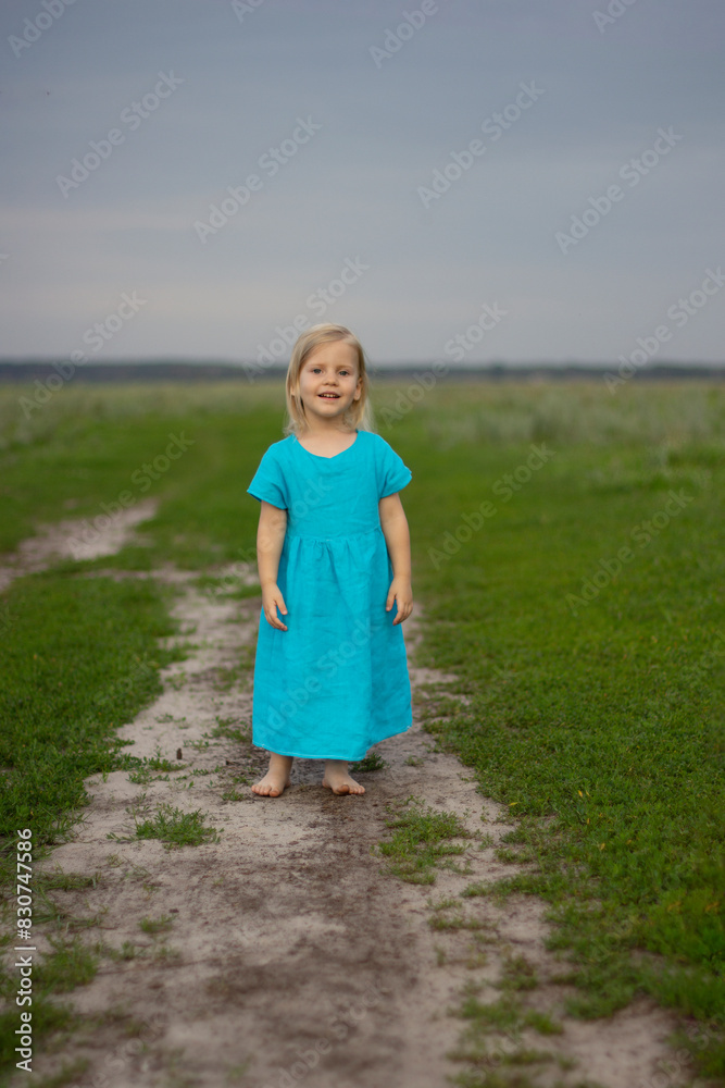 Little happy beautiful blonde girl in a blue linen sundress against the background of a green meadow, live emotions, smile. sunny day Little happy beautiful blonde girl in a blue linen sundress against the background of a green meadow, live emotions, smile. sunny day