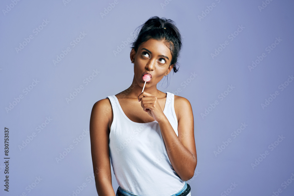 Woman, happy and thinking with lollipop in studio, summer and candy sweet for wellness with mock up space. Dessert, unhealthy snack and backdrop for treat idea, Indian female person and model Woman, happy and thinking with lollipop in studio, summer and candy sweet for wellness with mock up space. Dessert, unhealthy snack and backdrop for treat idea, Indian female person and model