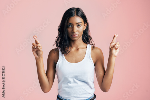 Hope, fingers crossed and portrait of woman in studio for optimism, pray or good luck sign. Serious, emoji and Indian female person with wish hand gesture for superstition isolated by pink background photo