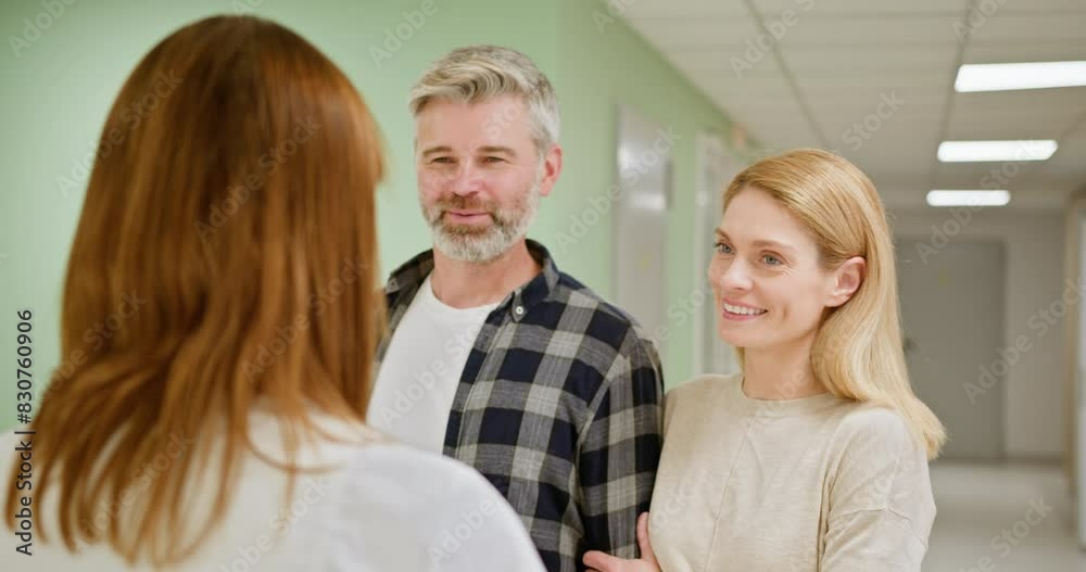 Receptionist talking to couple patients in front of reception counter in hospital. Man woman having conversation at reception. Family. Middle-Aged Couple at Hospital Consultation with Specialist. Receptionist talking to couple patients in front of reception counter in hospital. Man woman having conversation at reception. Family. Middle-Aged Couple at Hospital Consultation with Specialist.