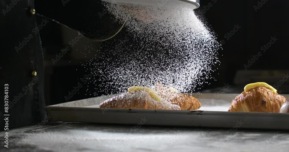 Super slow motion macro of professional artisan baker chef sprinkles sugar icing powder with sieve on homemade pastries sweet delicious dessert French croissants dessert in traditional bakery kitchen.