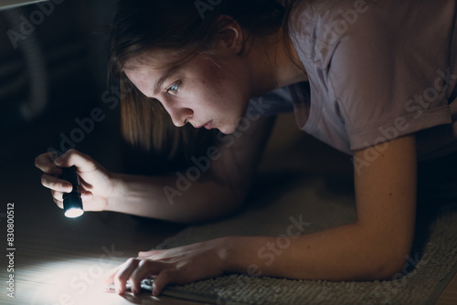 Woman young holding hand flashlight in darkness and search dirt spot on carpet