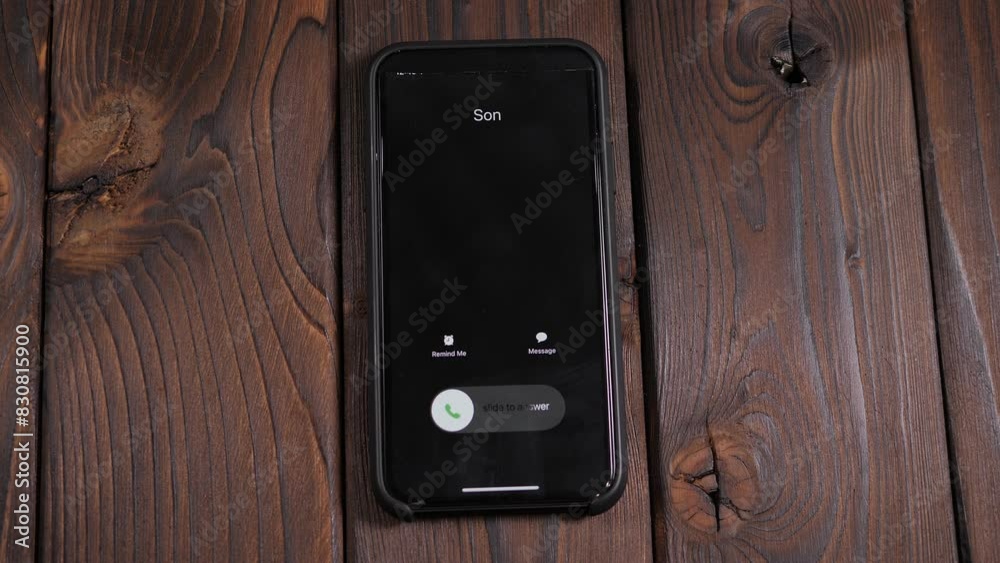 A close-up of an incoming call from his son on a smartphone screen on a wooden background, a man answers the call.