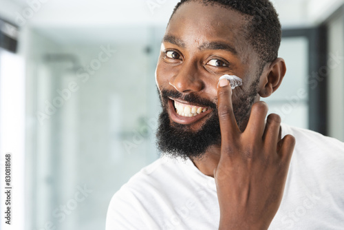 At home, African American man applying moisturizer, smiling at camera photo
