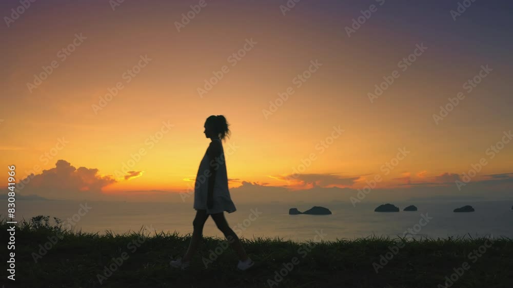 Woman walks hill edge, sunset in background, warm glow over landscape. Female enjoy aerial view on tropical island. Girl silhouette against colorful orange sky. Outdoor travel, summer holiday vacation Woman walks hill edge, sunset in background, warm glow over landscape. Female enjoy aerial view on tropical island. Girl silhouette against colorful orange sky. Outdoor travel, summer holiday vacation