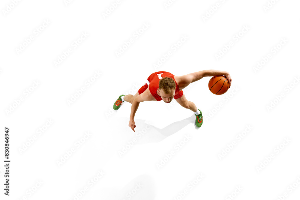 Aerial view of young athletic man, dressed red gear basketball player dribbling in motion against white studio background. Concept of professional sport, games, healthy lifestyle, tournament, action.