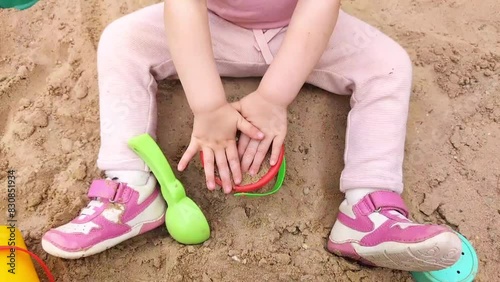 A child in pink clothes plays in the sandbox