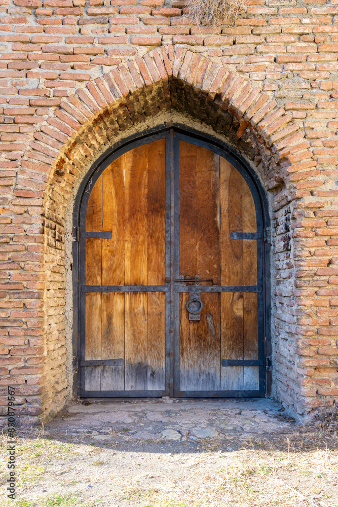 Old wooden door sheathed with iron ties, knocker, deadbolt and arched brick passage