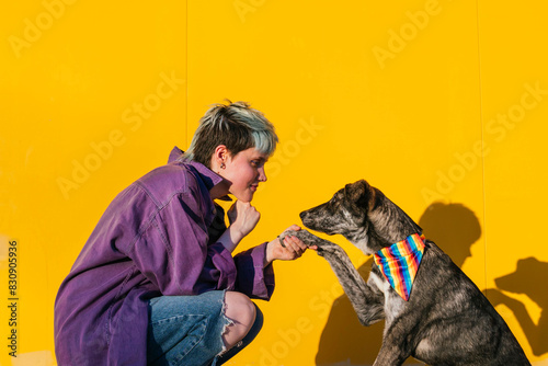 Lesbian woman holding dog's paw crouching in front of yellow wall