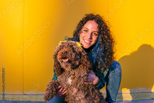 Smiling young woman spending leisure time with water dog in front of yellow wall photo