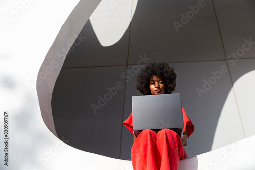 Woman with Afro hairstyle using laptop sitting on white wall