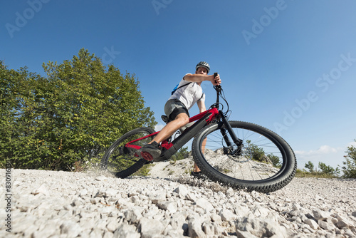 Male electric mountain bike rider going downhill and braking on a hilly rocky trail, low-angle shot. E-mountain biking concept. photo