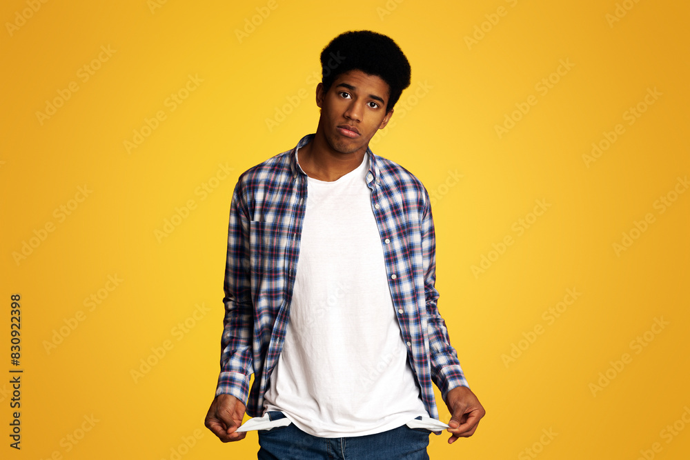 Poverty and Absence of Money. Unemployed Sad Afro Guy Showing Empty Pockets, Yellow Background Poverty and Absence of Money. Unemployed Sad Afro Guy Showing Empty Pockets, Yellow Background