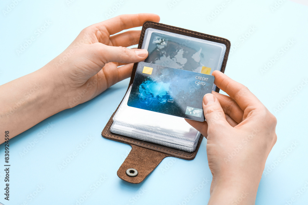 Woman holding leather card holder with credit cards on light blue background, closeup
