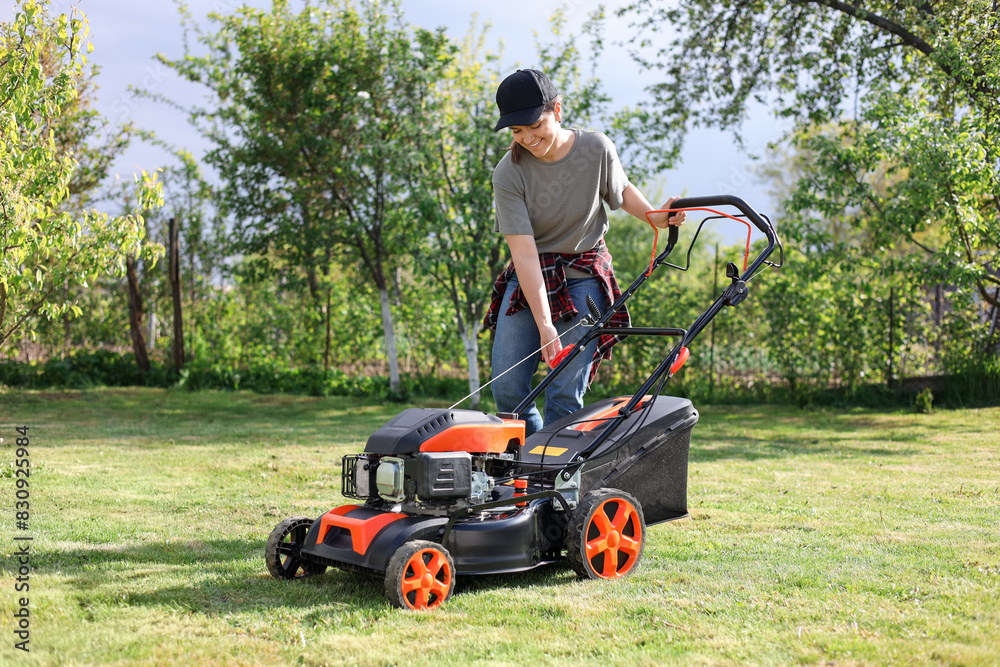 Smiling woman cutting green grass with lawn mower in garden Smiling woman cutting green grass with lawn mower in garden