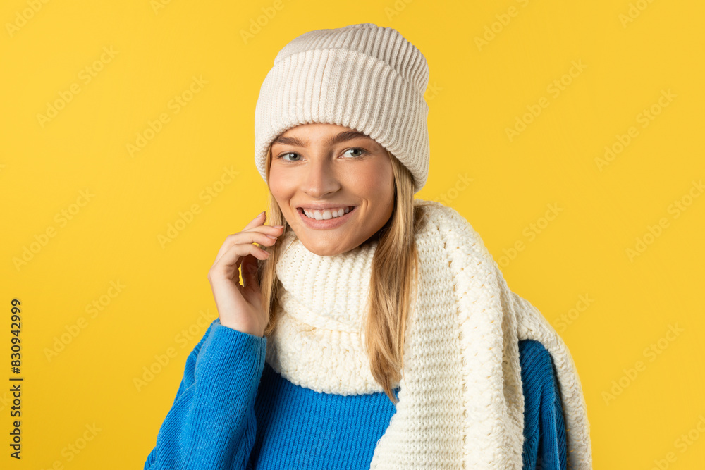 A woman dressed in a white hat and scarf stands outdoors. She is looking towards the camera, with a neutral expression on her face. The hat covers her head, and the scarf is wrapped around her neck A woman dressed in a white hat and scarf stands outdoors. She is looking towards the camera, with a neutral expression on her face. The hat covers her head, and the scarf is wrapped around her neck