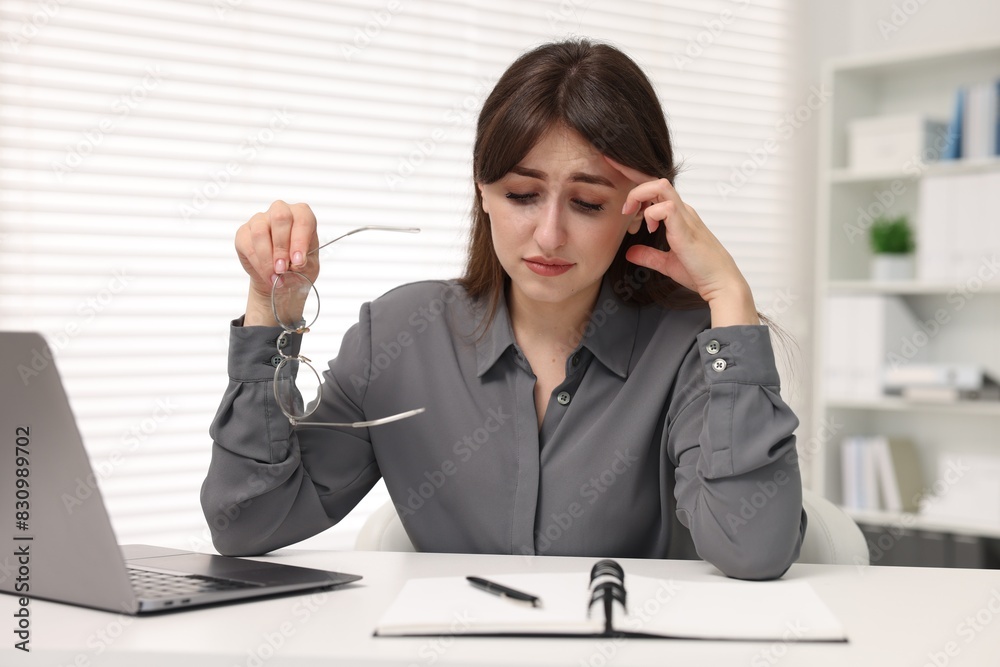 Overwhelmed woman sitting at table with laptop in office Overwhelmed woman sitting at table with laptop in office