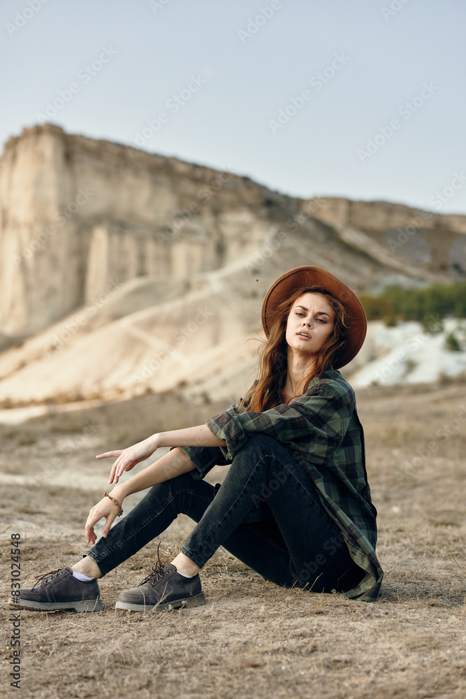 Serene young woman in hat sitting peacefully in front of majestic mountain landscape on sunny day Serene young woman in hat sitting peacefully in front of majestic mountain landscape on sunny day