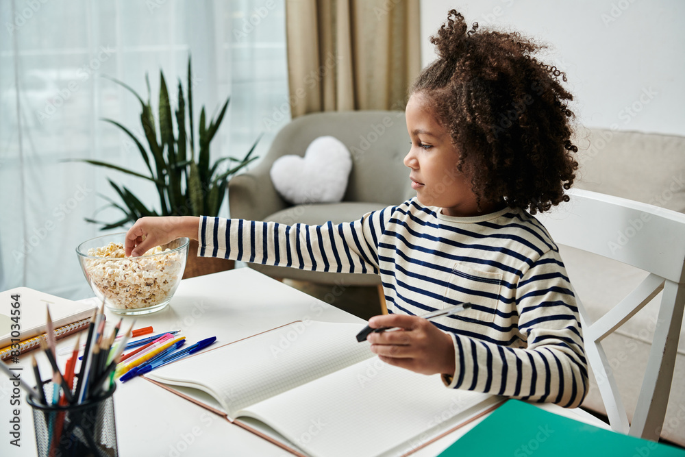 A little girl joyfully sits at a table, enjoying a bowl of popcorn A little girl joyfully sits at a table, enjoying a bowl of popcorn