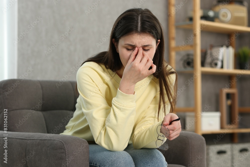 Overwhelmed woman with glasses sitting in armchair at home Overwhelmed woman with glasses sitting in armchair at home