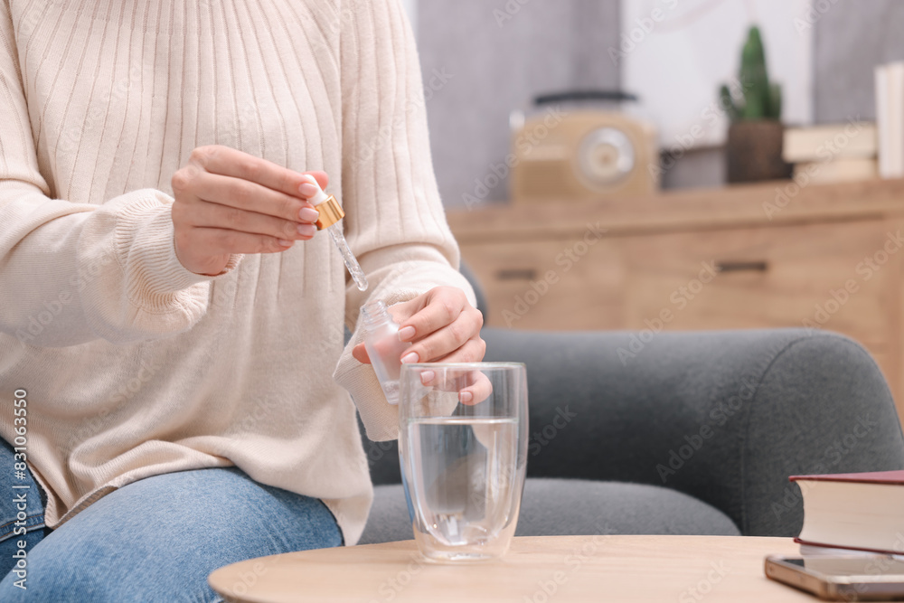 Woman dripping food supplement into glass of water on wooden table indoors, closeup. Space for text Woman dripping food supplement into glass of water on wooden table indoors, closeup. Space for text