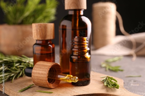 Fotografie Essential oil in bottles, dropper and rosemary on table, closeup