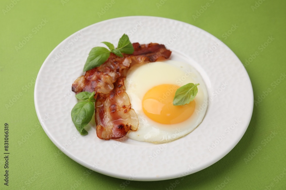 Fried egg, bacon and basil on green background Fried egg, bacon and basil on green background