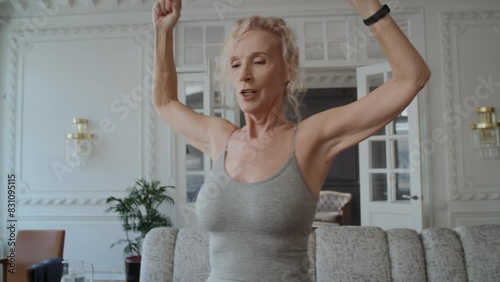 Senior attractive woman in 60s does sports activities. She is wearing fitness tracker on wrist to track progress and heart rate. The woman wants to stay active and healthy, using technology