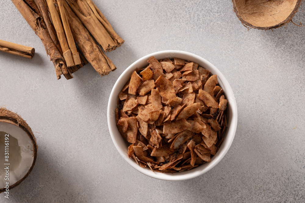 Coconut chips with cinnamon powder in bowl on gray background. Tasty sugar free snack. View from above. Coconut chips with cinnamon powder in bowl on gray background. Tasty sugar free snack. View from above.