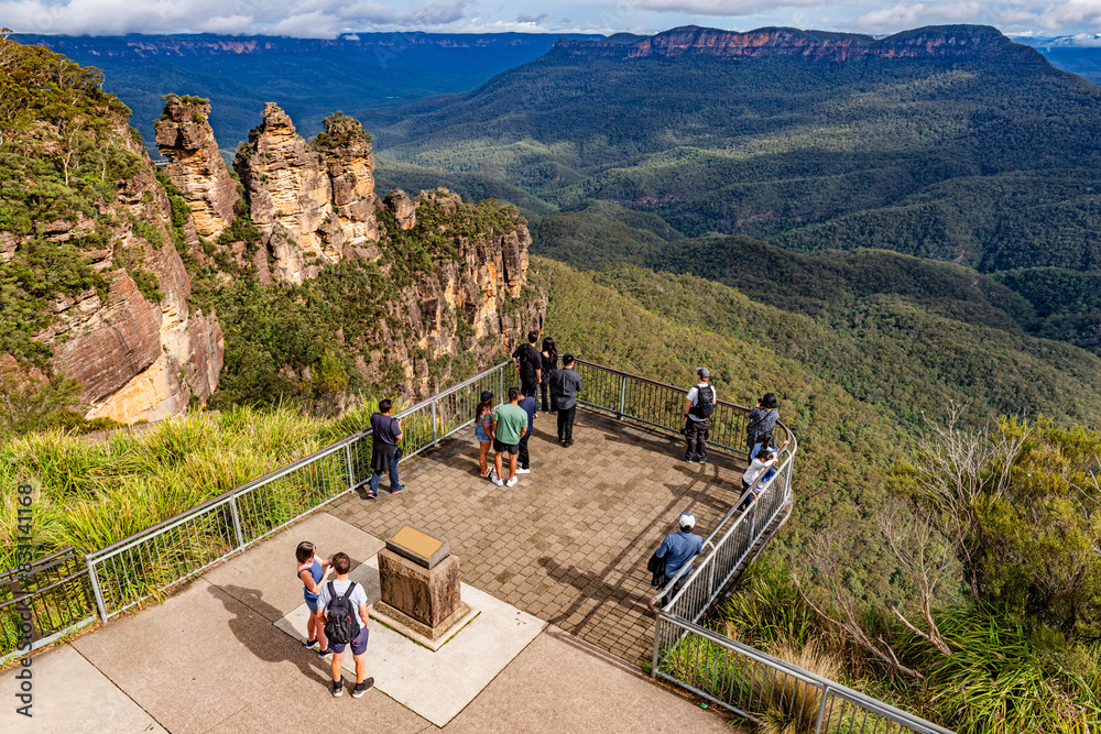 Fototapeta premium Tourists enjoy the view of the “Three Sisters” rock formation in the Blue Mountains National Park near Katoomba, NSW, Australia