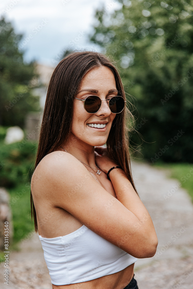 Smiling woman in sunglasses poses in front of trees Smiling woman in sunglasses poses in front of trees