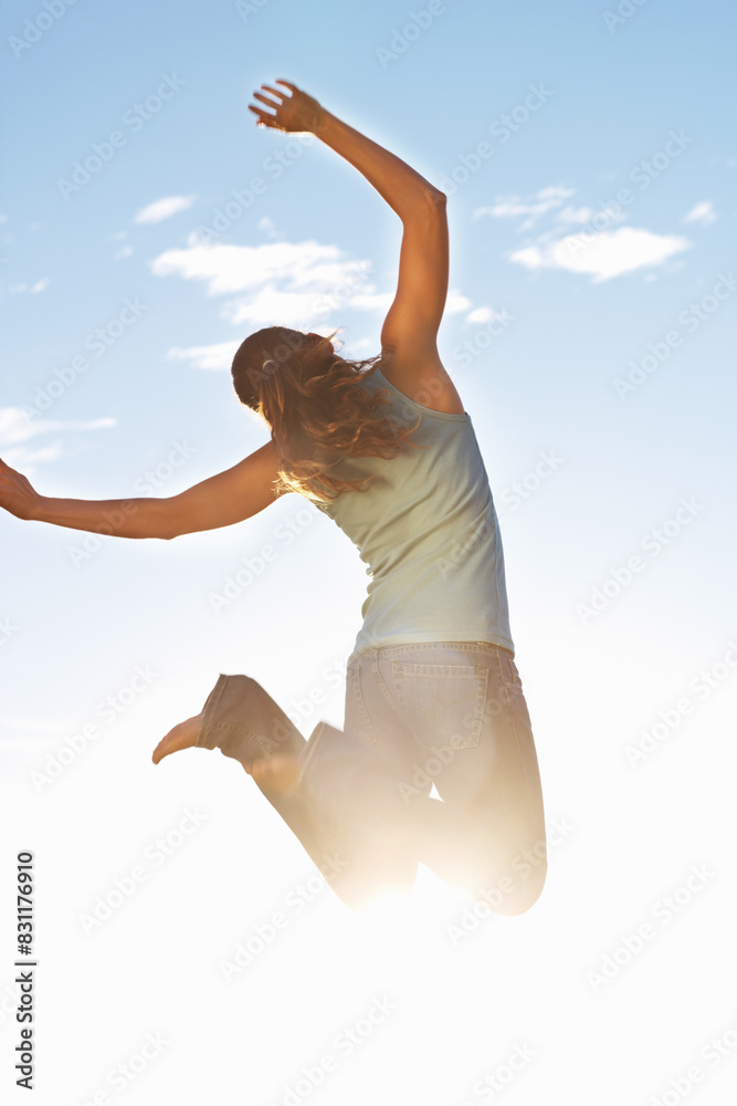 Fototapeta premium Back, happy woman and jump in nature for freedom, excitement and joy in sunshine. Female person, energy and arms up for success, achievement and celebrate outdoors in natural sunlight with bare feet