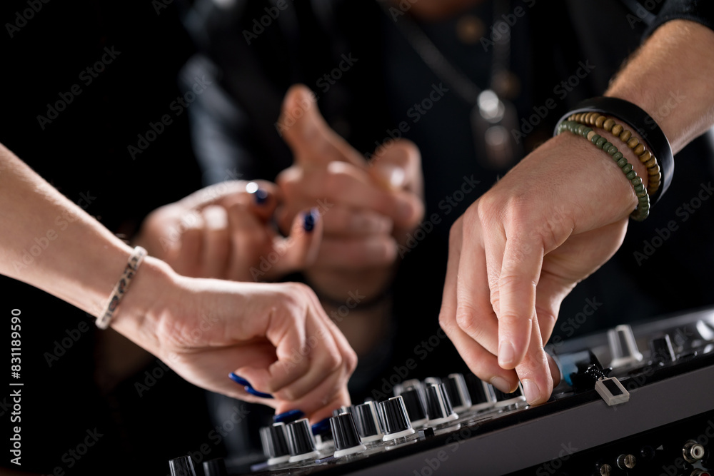 Hands adjusting knobs, DJ mixer, collaborative effort