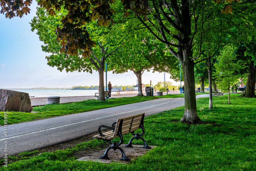 A wooden boardwalk a bike path, and an empty park bench  in Toronto's Beaches neighbourhood shot on an evening  in May