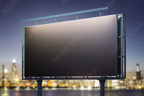 Blank black billboard on city buildings background at night, perspective view. Mockup, advertising concept photo