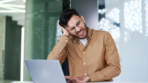 Earache. Sick businessman suffers from ear pain while sitting in business office. Upset man worker touches his ear with his fingers. He has furuncle, shingles, eczema, ear diseases or otitis media photo